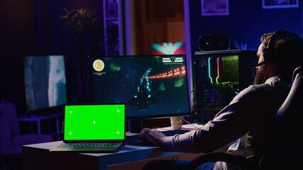 Green screen laptop next to man using gaming keyboard to play spaceship flying singleplayer game....