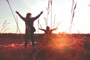 Child girl with mother in the meadow with raised hands, rear view. Relaxing. Summer sunset....