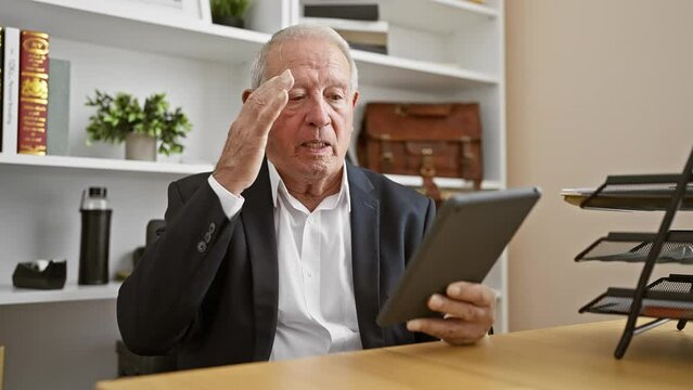 Upset senior man, a stressed business worker, frantically using touchpad at his office desk amid rising work problems - a portrait of worry on his mature face, white hair revealing his stressful job