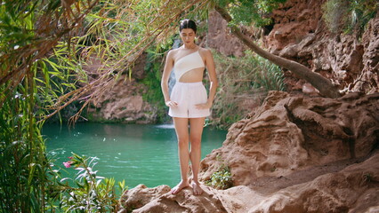 Meditative girl enjoying yoga on rocks sunny jungle nature. Woman raising hands
