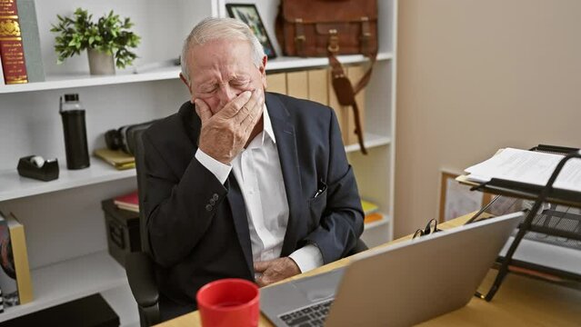 The struggle is real - senior business man forced to work sick at the office, displaying flu symptoms while slouched at his desk, amidst the deafening indoor silence.