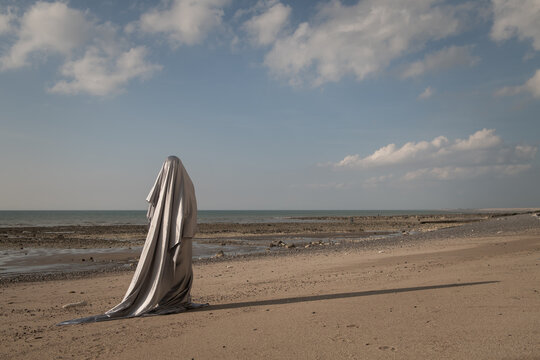 art portrait of woman in beach covered by silver shiny veil