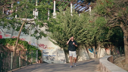 Fototapeta na wymiar Relaxed man calling mobile phone walking park alley. Guy holding tea laughing