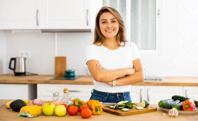 Obraz na płótnie Canvas Cheerful young Hispanic woman following healthy diet preparing vegetable salad for dinner in home kitchen