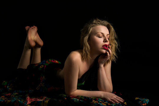 beautiful naked blonde girl with red lips in different colored Ukrainian traditional scarf on a black background lying on the floor