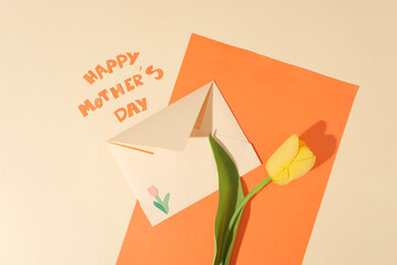 Orange paper decorated against beige background with a tulip flower and an envelope placed on....