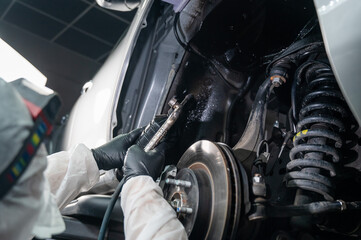 Fototapeta na wymiar An auto mechanic applies anti-corrosion mastic to the underbody of a car.