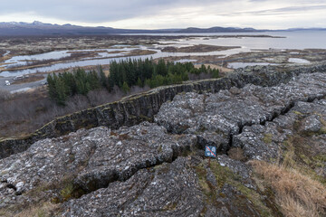 natural tectonic landscape of Thingvellir National Park, with sign 'stepping the tectonic crack is...