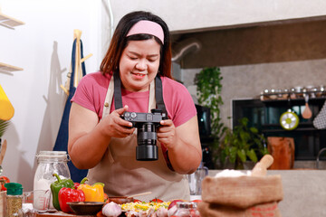 Cute Asian fat girl is happy cooking in the kitchen at home. She held a camera and took pictures of her finished food. Fast food. Pizza - obrazy, fototapety, plakaty