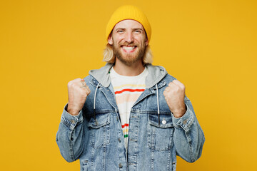 Young happy blond man wears denim shirt hoody beanie hat casual clothes doing winner gesture celebrate clenching fists say yes isolated on plain yellow background studio portrait. Lifestyle concept.