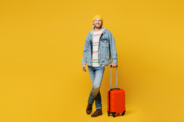 Traveler happy man wear denim casual clothes hold suitcase bag look camera isolated on plain yellow background. Tourist travel abroad in free spare time rest getaway. Air flight trip journey concept.