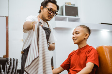 asian professional male hairdresser putting a cape on his customer with serious expression