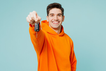 Young man wears orange hoody casual clothes hold in hand car key fob keyless system stretch hand to camera isolated on plain pastel light blue cyan color background studio portrait. Lifestyle concept.