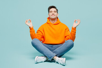 Full body young man wear orange hoody casual clothes sitting hold spreading hands in yoga om aum...