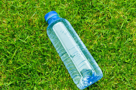 bottle on the grass. blue transparent small bottle with water lies on a green azon top view close up