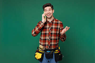 Young happy employee laborer handyman man wear red shirt talk speak on mobile cell phone isolated on plain green background. Instruments accessories for renovation apartment room. Repair home concept.