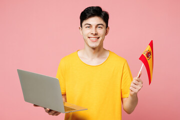Young smiling student IT man he wears yellow t-shirt casual clothes hold Spanish flag use work on...