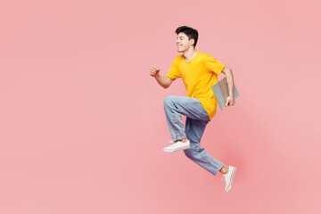 Fototapeta na wymiar Full body young IT man he wear yellow t-shirt casual clothes jump high hold closed laptop pc computer run fast isolated on plain pastel light pink color background studio portrait. Lifestyle concept.