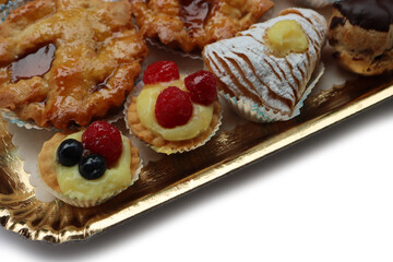 Traditional assortment of italian pastries on golden tray. Cannoli, Babà, cream puffs, small pies with jam, mini tart with cream and fruits and apple pie