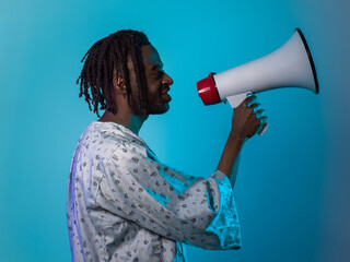 African American man dons traditional attire, passionately utilizing a megaphone against a striking blue background, symbolizing his vocal and cultural empowerment in the pursuit of social justice and