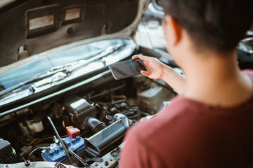 male mechanic takes cell phone photo of car engine while repairing car