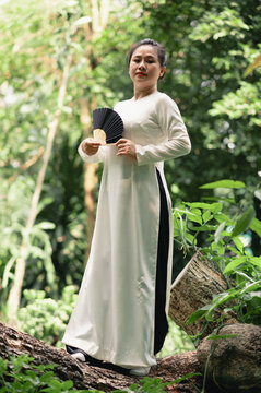 Portrait of Vietnamese woman in white ao dai resting near the lake in the park