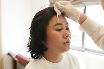 Young asian woman undergoing eyebrow correction procedure in beauty salon, closeup