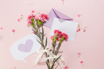 Fresh carnation branches are decorated with ribbons tied in bows, next to a pastel purple envelope...