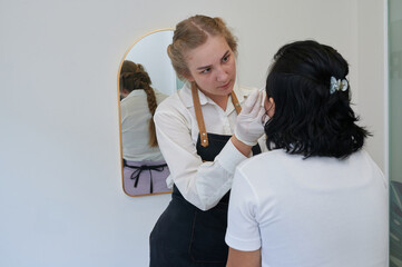 Young Asian woman undergoing eyebrow correction procedure in beauty salon, closeup