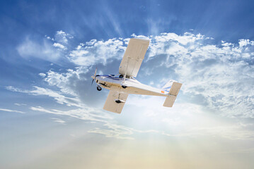 Single engine ultralight plane flying in the blue sky with white clouds	