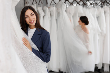 Two beautiful bridesmaids of a friend choose a wedding dress in the salon, have fun and laugh....