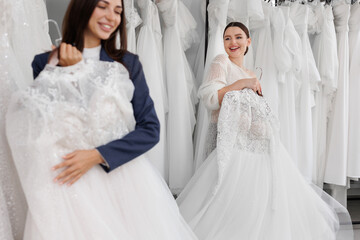 Two beautiful bridesmaids of a friend choose a wedding dress in the salon, have fun and laugh....