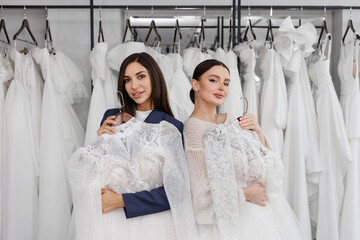 Two beautiful bridesmaids of a friend choose a wedding dress in the salon. Preparing for the...