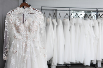 Many luxurious expensive wedding dresses are hanging on hangers in the wedding salon, shop.
