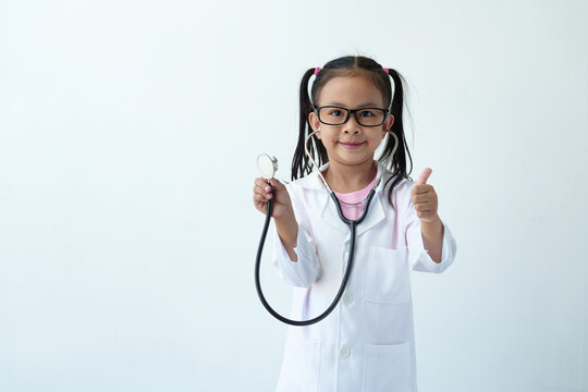 A girl wearing a doctor's uniform, standing with smiling glasses and a stethoscope is playing a doctor. and give a thumbs up showing excellent work, excellent, on a white background.