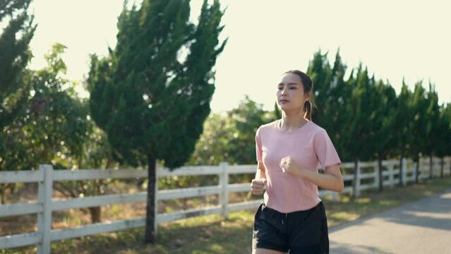 Happy thin woman wearing sports clothes jogging at the park at sunrise Beautiful young Asian woman in exercise clothes running outdoors. Morning exercise The concept of a healthy and active lifestyle