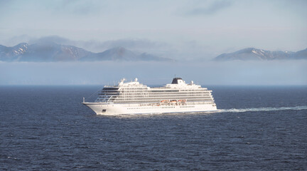 a small white cruise ship sails near Iceland on a cloudy and foggy summer day with mountains in the...