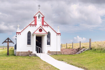 small ornate Catholic chapel tourist attraction on Orkney islands in Scotland with a mowed lawn in front and a cross with Jesus on the side