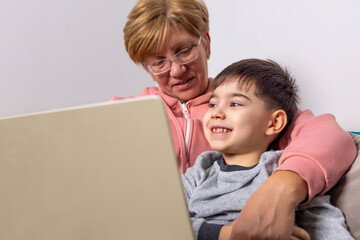 beautiful older granny and nephew sitting on sofa in front of laptop,talking to someone. grandmother old female lady with vision glasses on eyes and smiling kid child boy. togetherness concept 4k