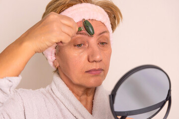 elder woman granny is using gua sha and jade roller for facial massage. anti wrinkle...