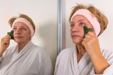elder woman granny is using gua sha and jade roller for facial massage. anti wrinkle...