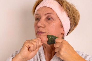 elder woman granny is using gua sha and jade roller for facial massage. anti wrinkle...