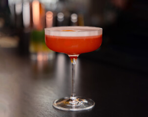 cocktail in glass on bar counter against cozy moody lights in background. pink grapefruit cocktail or fresh yellow with dry ananas and leaf decor. party concept, weekend evening fun.