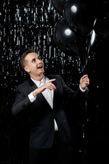 Happy handsome guy in black jacket holding black air balloons on glitter background. male birthday