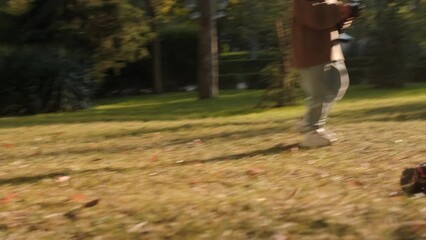 A boy stands in a sunlit clearing in a park and plays with a remote control car that moves quickly through the grass around him. Outdoor games, radio controlled toys, childhood.