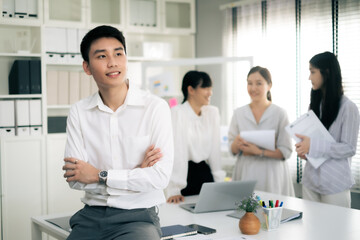 Young Asian business man cross arm at chest looking away with smile of confident, co-worker blur background.