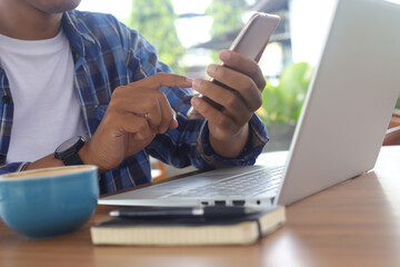 Fototapeta premium Close up of freelance male hand working on laptop while using a mobile phone. Business and mockup concept