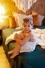 Cute child, boy, sitting at home in bed after shower