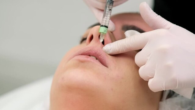 A cosmetologist makes injections into the lips of a beautiful girl. Procedure for lip augmentation, cosmetic services and injection plastic surgery.
