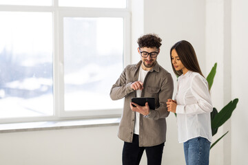 Two young businesspeople using a digital tablet while standing in a boardroom.